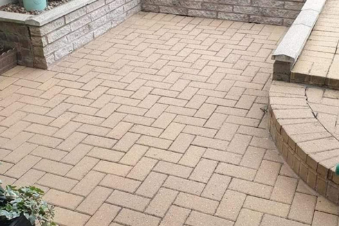 stone patio with herringbone patterned pavers in outdoor space surrounded by low walls and greenery 2 ways to enhance outdoor areas